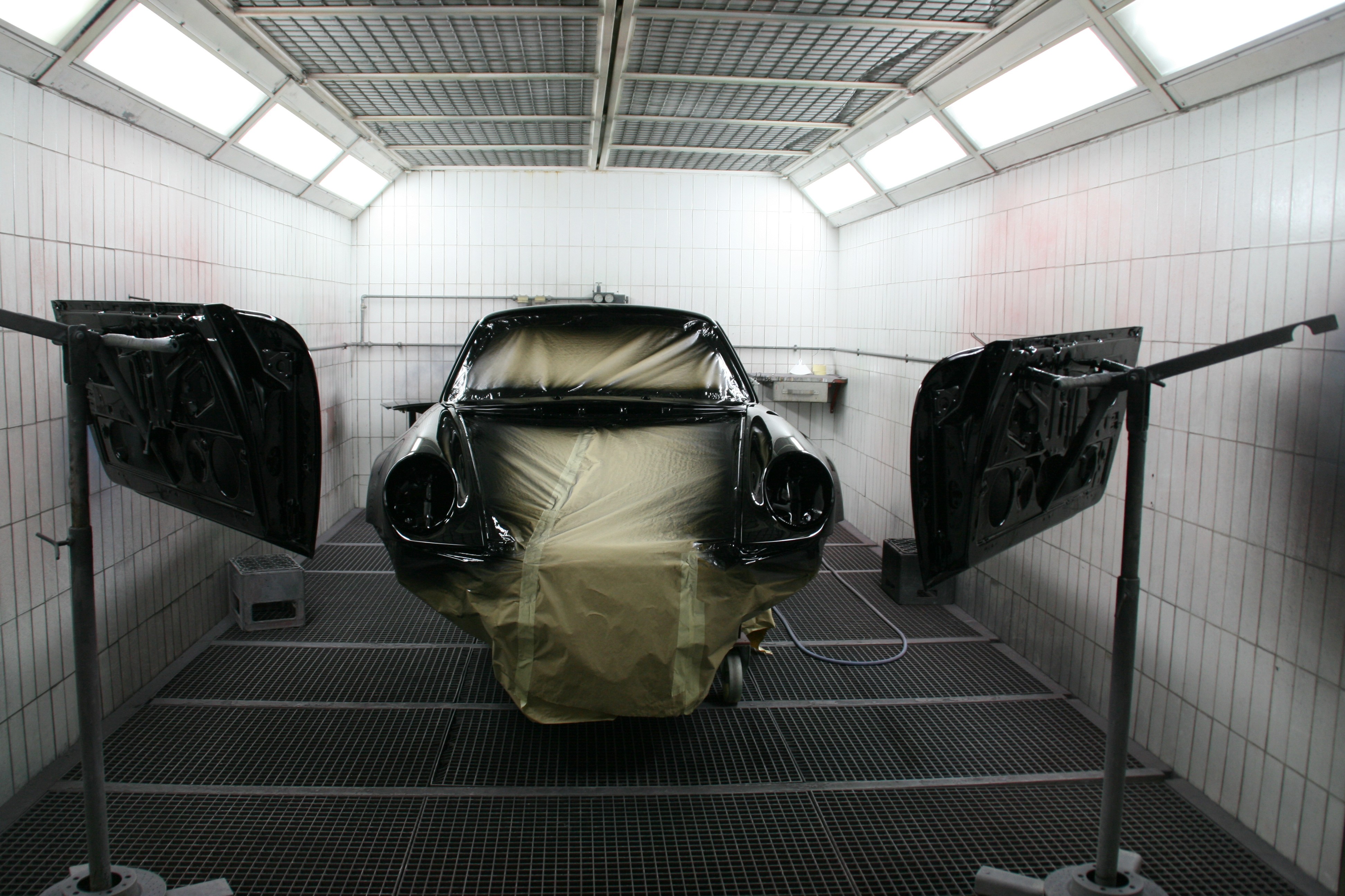 Car body and detached panels masked for refinishing in a paint booth